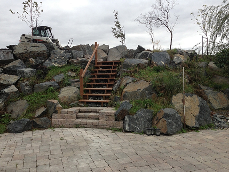 Back yard hill with built-in staircase and black granite boulders. Roman paver patio in Antique brown.