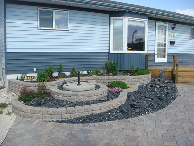 Multi-tier Roman Stack Stone planter with plants and crushed black granite. Roman paver walkway leading to treated green front deck