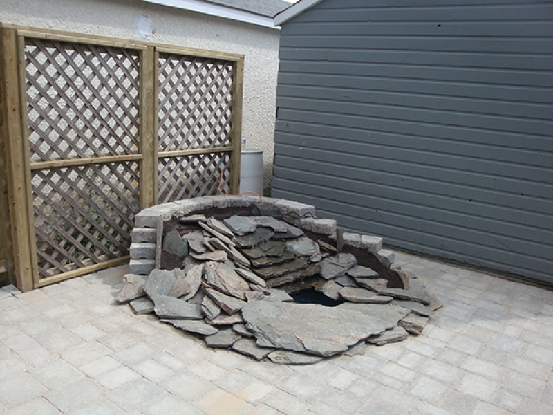 Pond and waterfall built into Roman paver patio. Treated green lattice privacy wall backdrop.