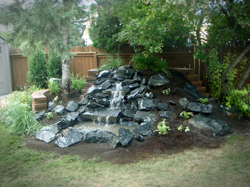 Black granite waterfall with soil and plantings. Supported from behind by a Roman Pisa retaining wall in Autumn Brown