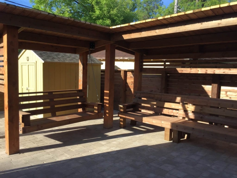 Treated brown pergola with hanging bench, fixed bench, Roman paving stones, planter with trellis, etc