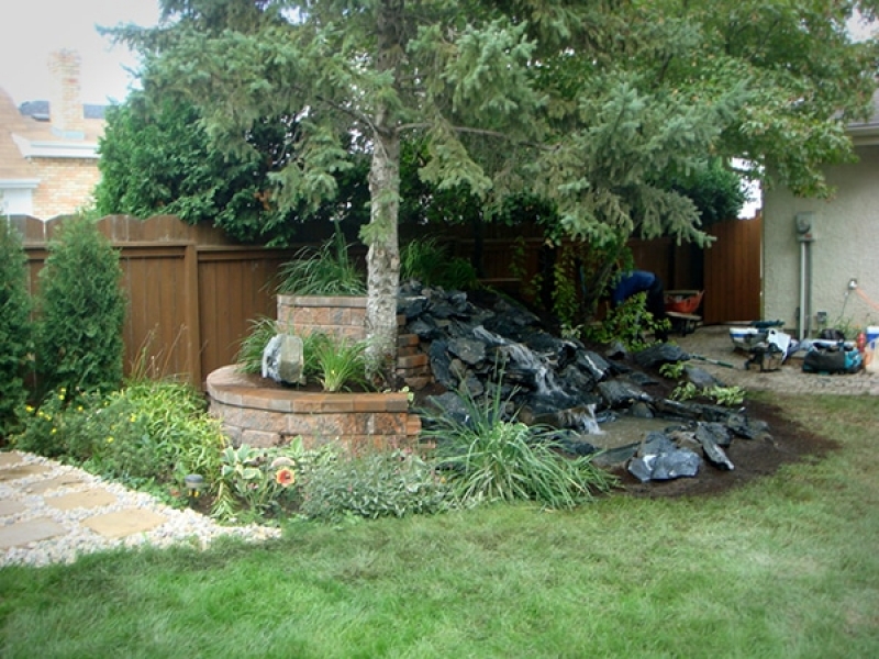 Black granite waterfall with soil and plantings. Supported from behind by a Roman Pisa retaining wall in Autumn Brown