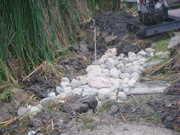 Boulders being installed to reduce erosion by man made lake rock gardens grading and drainage