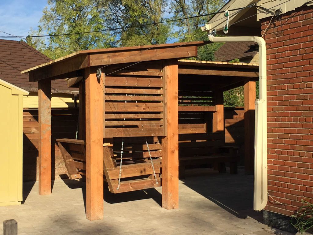 Treated brown pergola with hanging bench, fixed bench, Roman paving stones, planter with trellis, etc